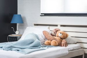 Senior man asleep in bed with teddy bear.