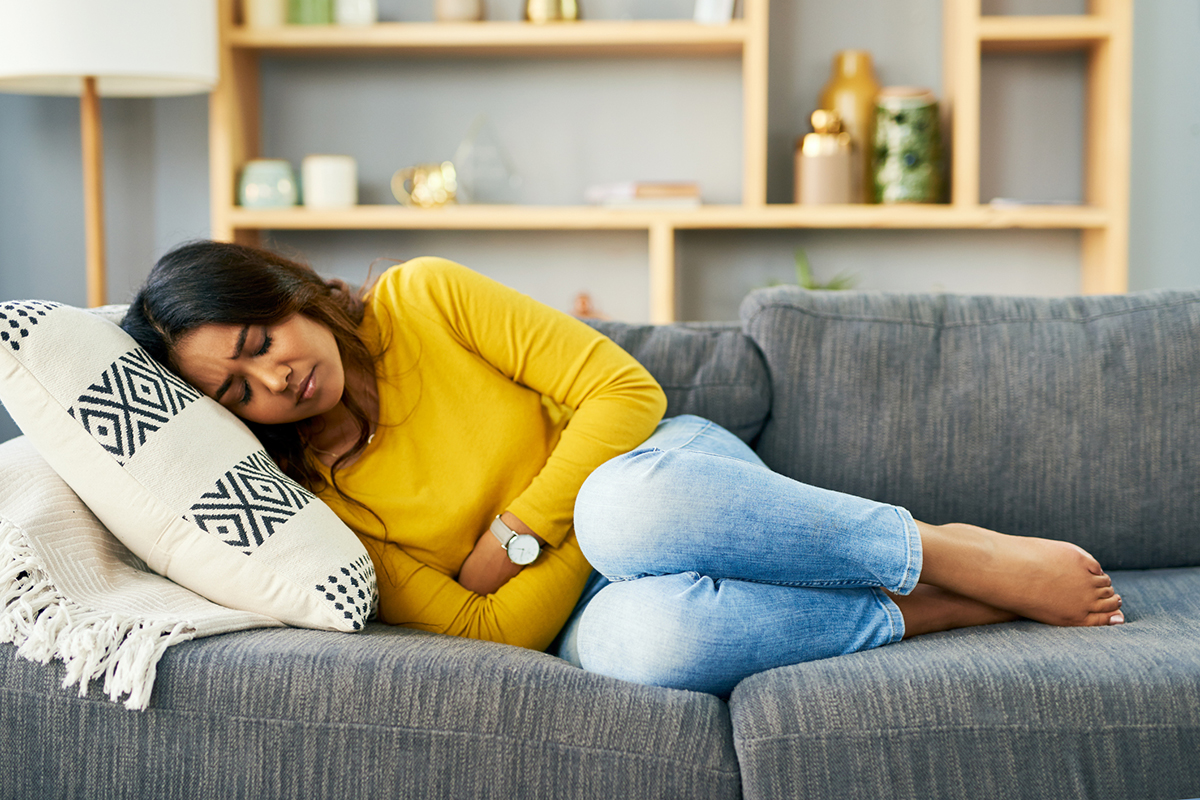 Woman laying on couch with her arms wrapped around her midsection