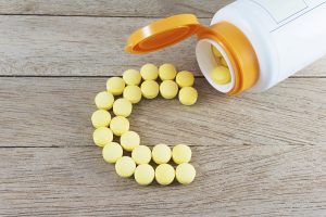 Vitamin C pills arranged in the shape of the letter C next to an open pill bottle