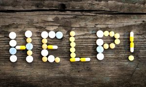 The word "HELP!" spelled out in pills on a wooden background