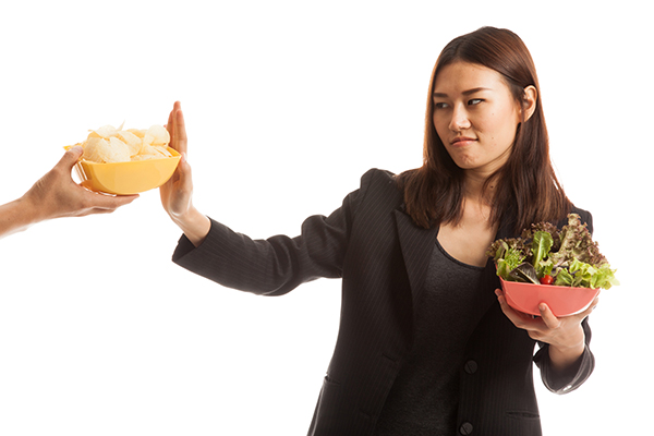 Young Asian woman holding a salad in one hand and rejecting potato chips with the other