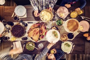Overhead view of a table laid with a holiday feast. Guests pass dishes to each other.