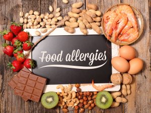 Blackboard sign reading "food allergies" surrounded by common allergenic foods such as nuts, eggs, and shellfish.