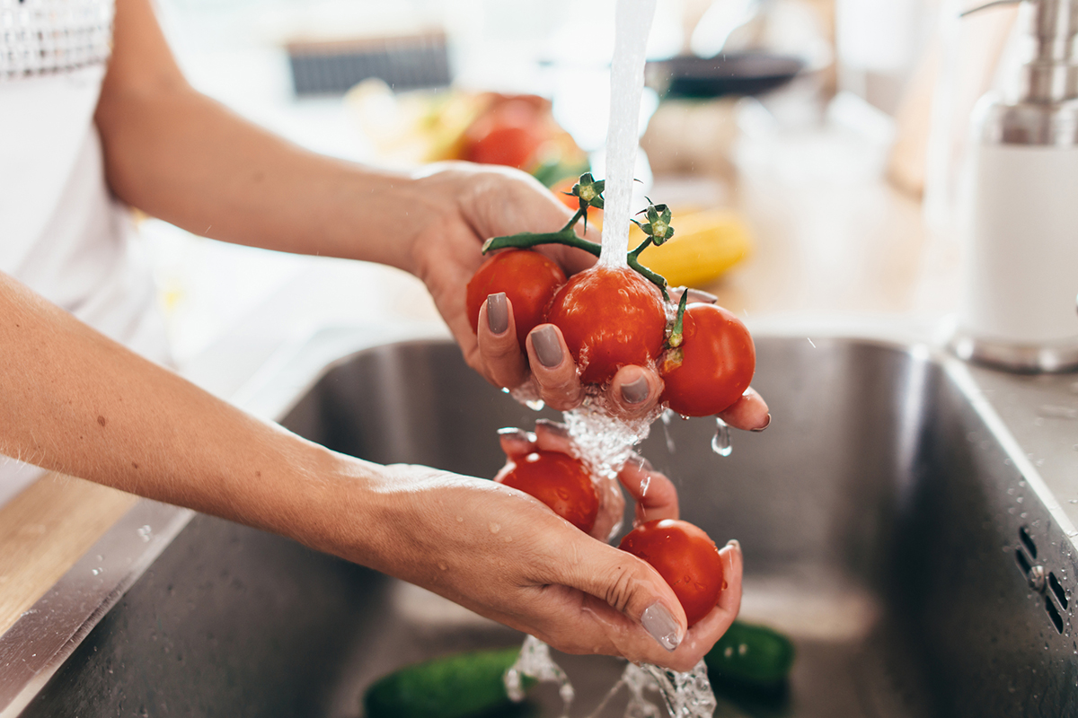 A woman rinsing small tomatoes on the vine in her kitchen sink.