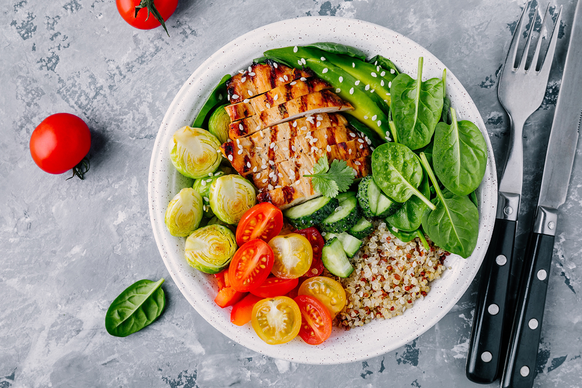 Grain bowl with quinoa, grilled chicken, tomatoes, cucumbers, spinach, and avocado