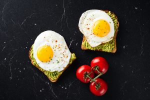 Two pieces of toast with sunny side up eggs on top, next to three small tomatoes on the vine.