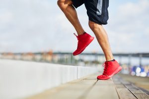 A close up shot of an athletic man running up stairs. He's wearing red running shoes and blue shorts.