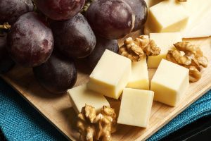 Close up photo of grapes, cubed cheese, and walnuts on a wooden platter