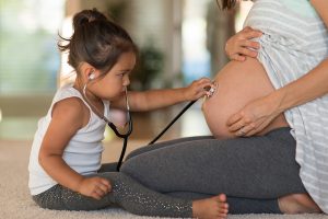 A little girl holding a stethoscope on her mother's pregnant belly