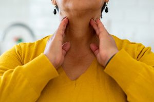 Close up of woman pressing her fingers along both sides of her neck to feel her thyroid.