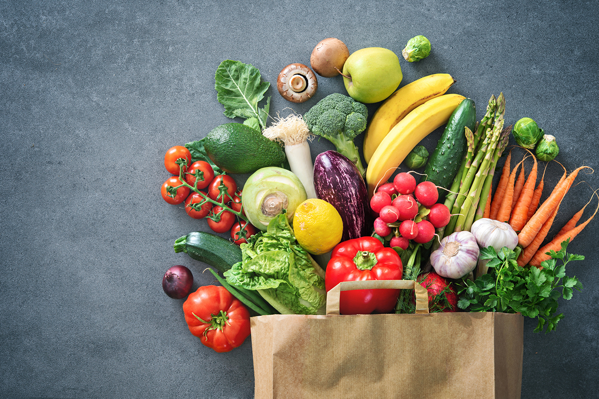 A brown paper grocery bag with an assortment of produce spilling out onto a concrete counter.