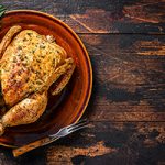 Whole roasted chicken on a plate with utensils on a wooden background