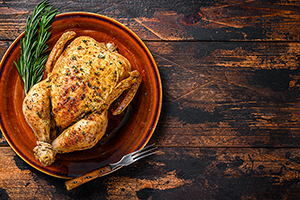 Whole roasted chicken on a plate with utensils on a wooden background
