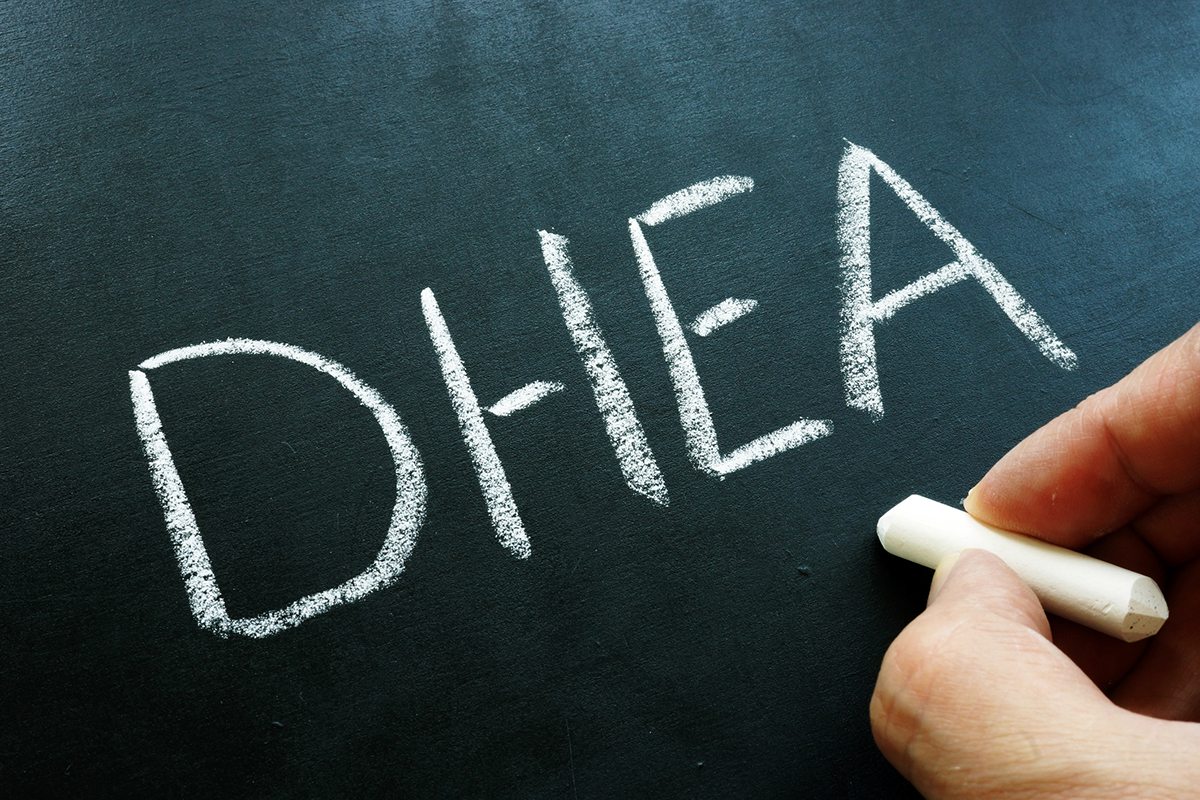 Hand writing "DHEA" in chalk on a blackboard