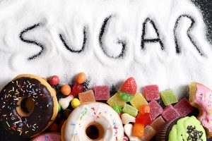 The word "sugar" written in a spill of table sugar, with an array of donuts and candy at the bottom of the picture.