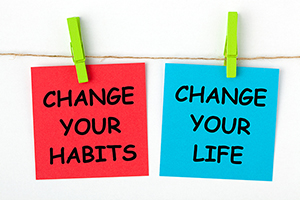 Two pieces of paper clipped onto a line with a wooden pin. A red square reads CHANGE YOUR HABITS, and blue square reads CHANGE YOUR LIFE