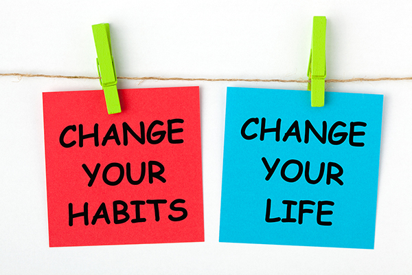 Two pieces of paper clipped onto a line with a wooden pin. A red square reads CHANGE YOUR HABITS, and blue square reads CHANGE YOUR LIFE
