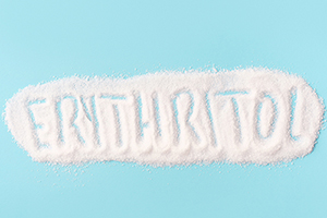 "Erythritol" inscribed in a spill of white erythritol powder on a blue background