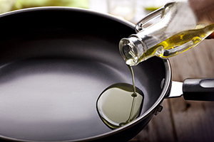 Cooking oil being poured from a glass bottle into a frying pan