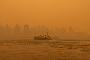 A barge boat traveling on the East River in New York City with a sky filled with massive air pollution from wildfires