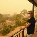 A woman, on a balcony, wears a face mask to protect herself against very dangerous level of air pollution. A thick yellow fog coming from the nearby forest fires covers Canberra city.