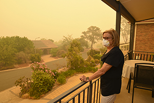 A woman, on a balcony, wears a face mask to protect herself against very dangerous level of air pollution. A thick yellow fog coming from the nearby forest fires covers Canberra city.