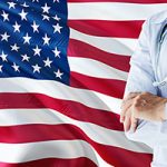 Doctor standing with stethoscope on United States flag background.