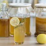 Kombucha tea with lemon and sweetened root filling in glass jug on kitchen background.
