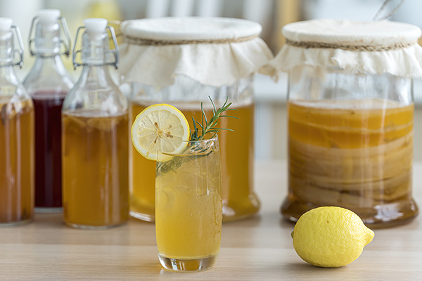 Kombucha tea with lemon and sweetened root filling in glass jug on kitchen background.