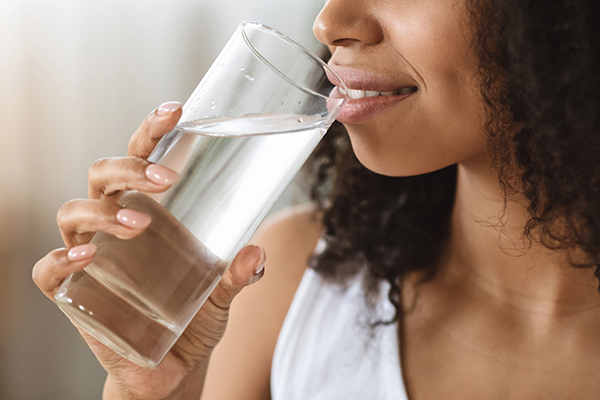 Black woman in white tank top drinking water from a tall glass