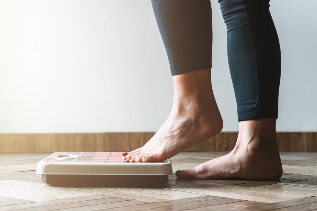 Barefoot woman in black legging stepping one foot into a scale