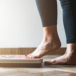Barefoot woman in black legging stepping one foot into a scale