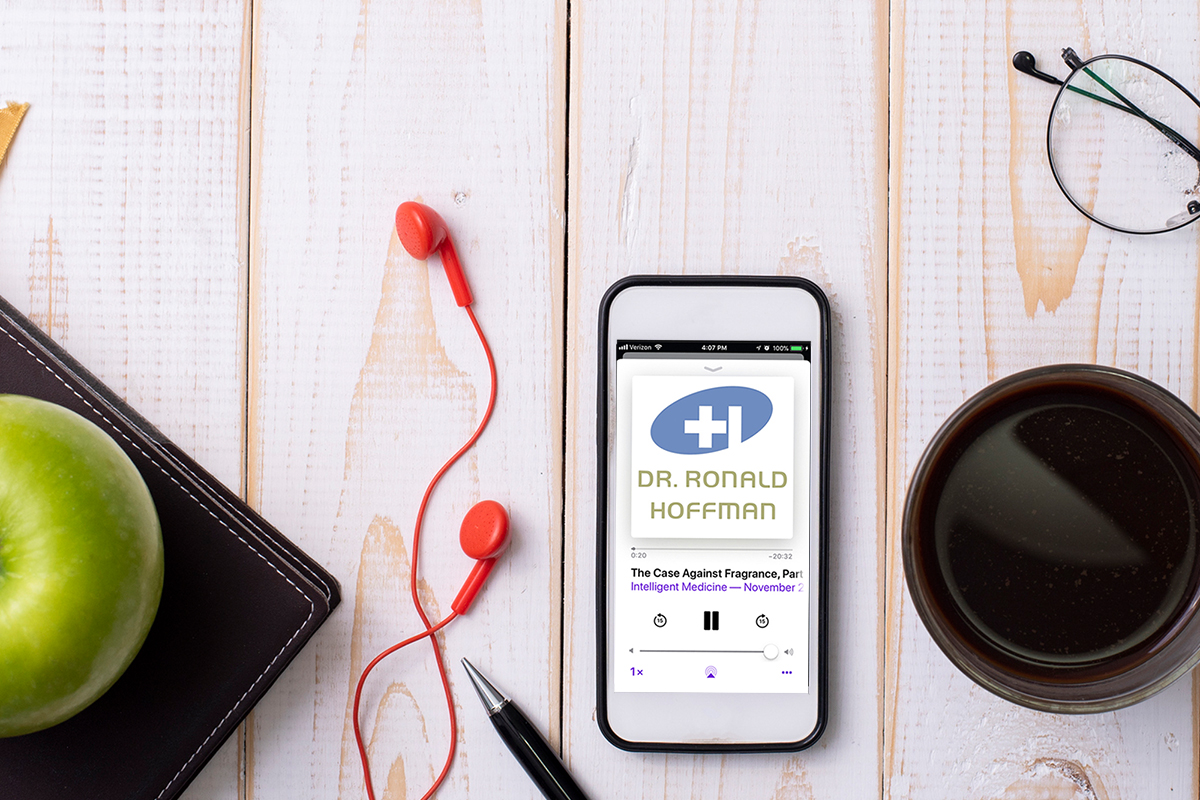 A smartphone playing the Intelligent Medicine podcast sits atop a wooden surface, along with wired earbuds, a cup of coffee, a leather-covered journal and a green apple.