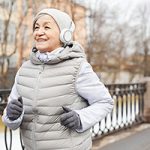 Waist up portrait of active senior woman running outdoors in winter and smiling happily
