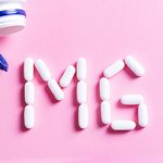 Pink background with an open pill bottle in the top left. Below it, white pill capsules spell out MG for magnesium.