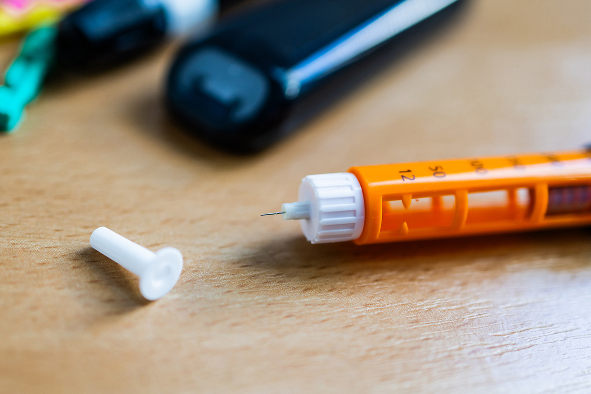 Uncapped insulin pen in the foreground with a glucometer in the background.