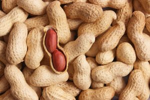 A background of peanuts in the shell. One is cracked open and missing half the shell, revealing two peanuts inside.