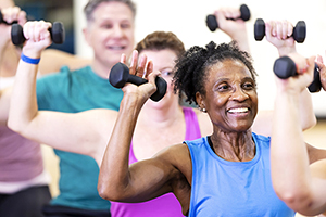 Close-up of a senior African-American woman in her 60s enjoying an exercise class. She is with a multiracial group of mature adults sitting on fitness balls and lifting hand weights.