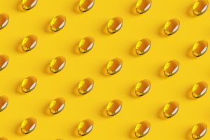 Rows of golden fish oil capsules on yellow background.