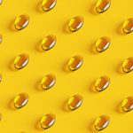 Rows of golden fish oil capsules on yellow background.