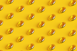 Rows of golden fish oil capsules on yellow background.