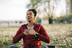 African American woman taking deep relaxing breaths while sitting cross-legged outdoors.