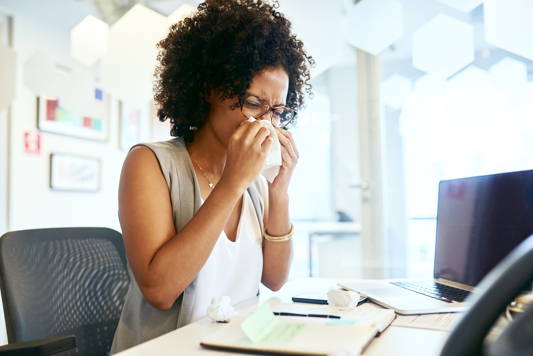 African American woman blowing her nose while sitting at her desk