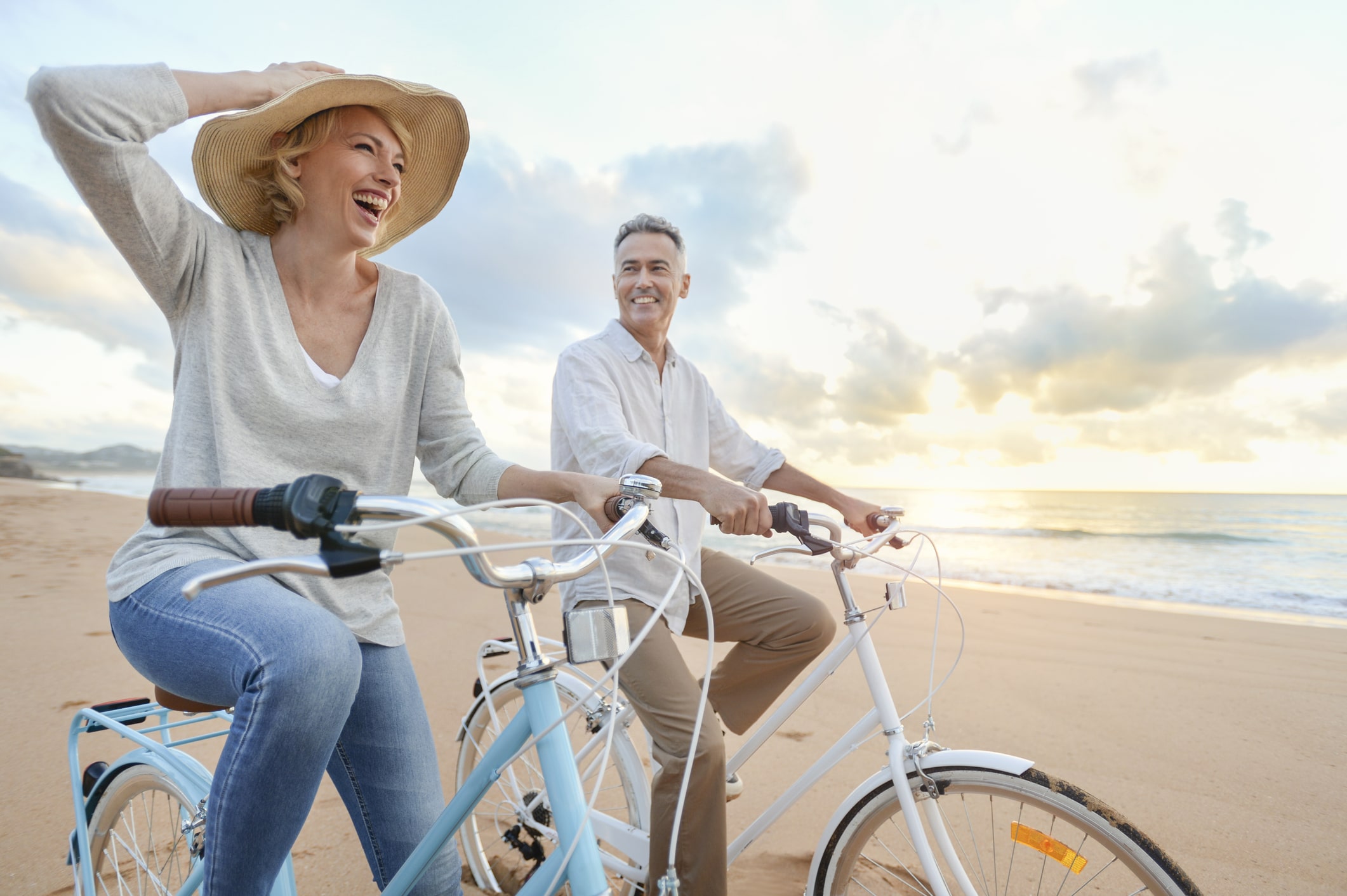 Mature couple cycling on the beach at sunset.