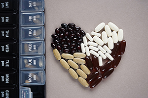 Supplements and tablets laid out in heart shapes next to the pillbox by day on a gray background