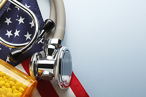 A prescription medication bottle and a stethoscope rest on top of an American flag.