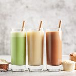 A trio of protein shakes with straws, along with measuring scoops of protein powders.