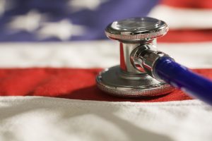 Social and political issue of healthcare and medicine changes and reform in USA politics and policies, symbolized by a close-up of a stethoscope resting on a the cloth fabric of the United States flag.