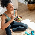 Shot of athletic woman eating a healthy fruit bowl while sitting on floor in the kitchen at home