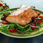 Baked salmon steak with tomato, onion, mix of green leaves salad in a plate. healthy food.